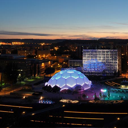 Vista aérea de la ciudad con la cúpula de la plaza milenio con fachada ETFE de noche iluminada en az